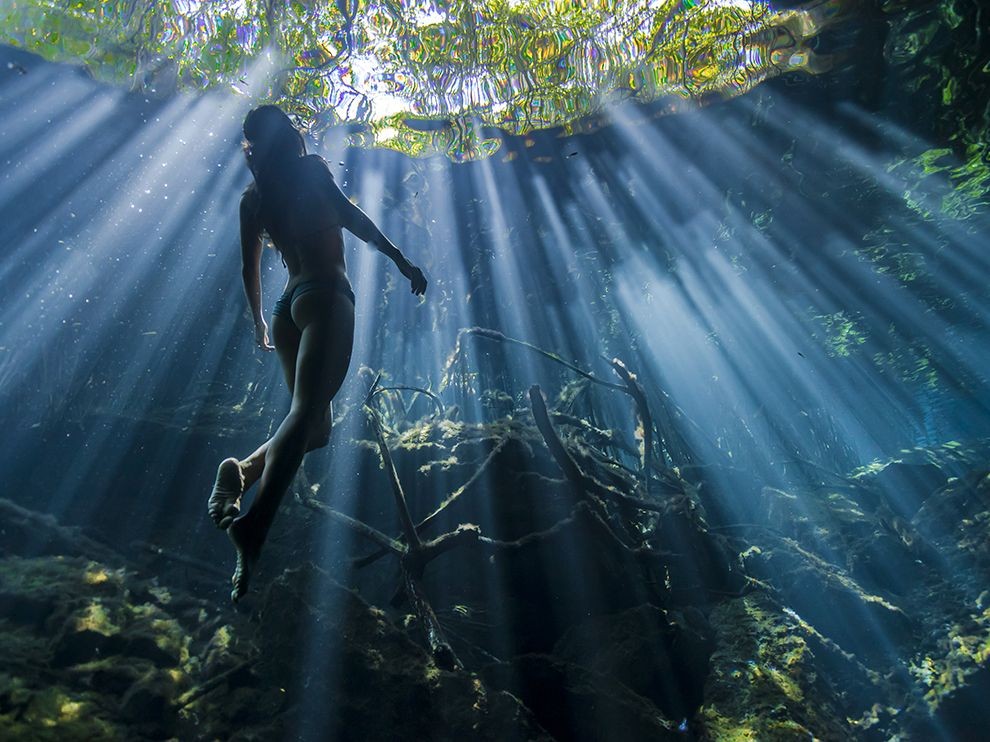 Quintana Roo, Mexico: Ánh mặt trời xuyên qua làn nước trong vắt của hố sụt Cristalino ở Quintana Roo khi một cô gái đang bơi lên mặt nước. Người Maya tin rằng các hố sụt này là lối đi bí mật tới cõi của người chết. Ảnh: Christian Vizl.